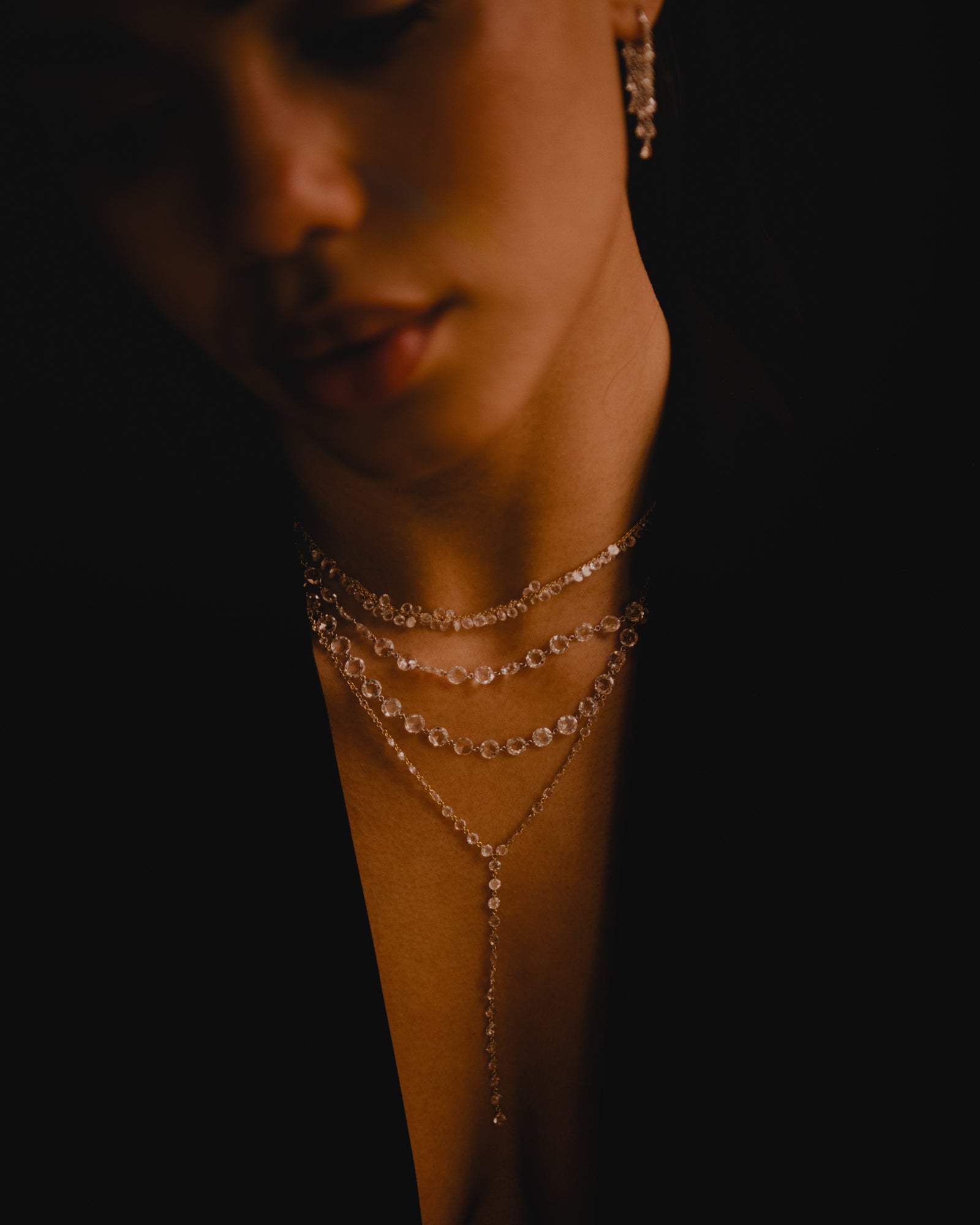 Beautiful model's face and neck wearing layers of rose cut diamond jewelry from Eleuthera Zo's Amóre collection. 3 necklaces made of rose cut diamonds and 18k yellow gold and 1 rose cut dimaond lariat. Rose cut dangling diamond earrings.