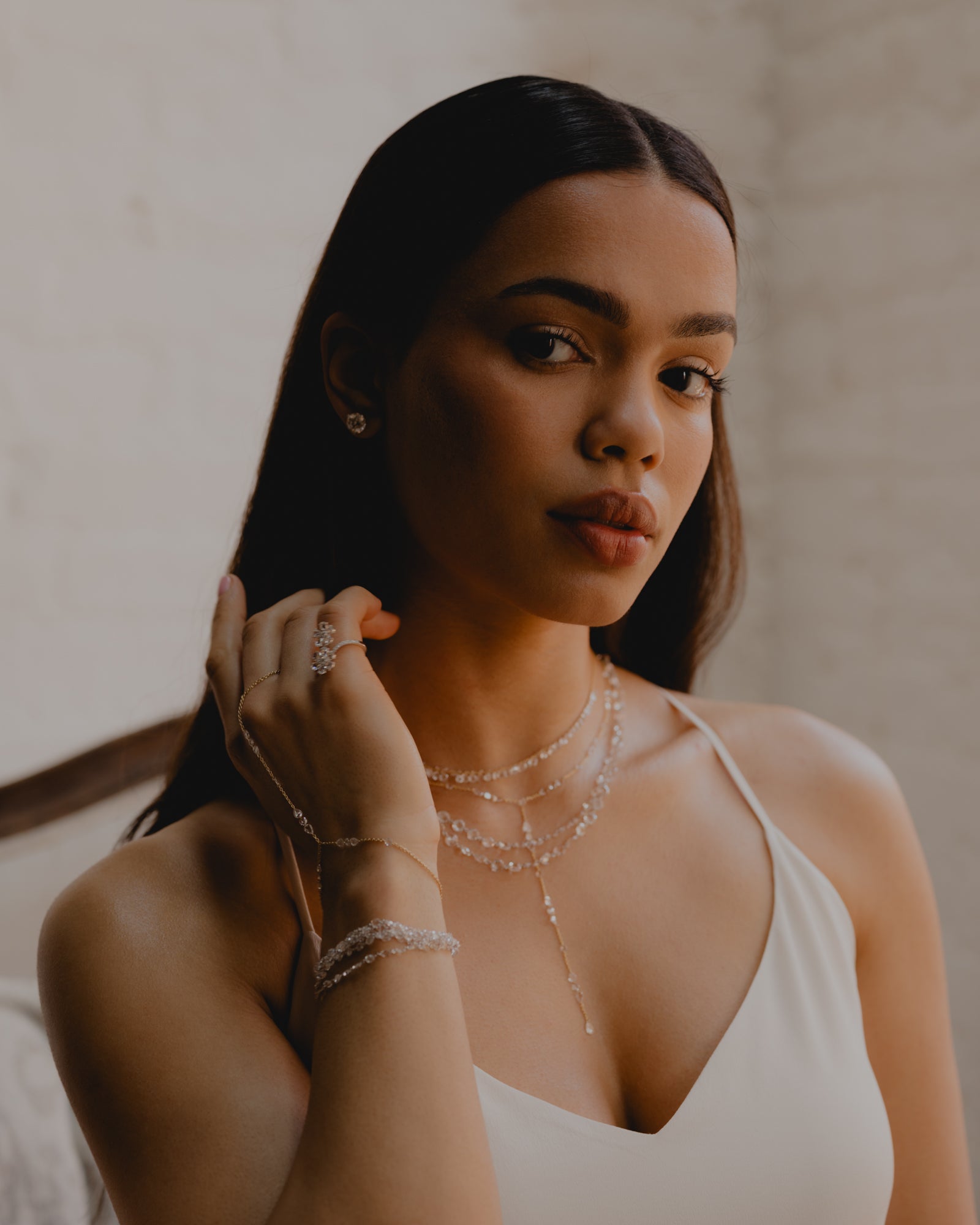 Woman wearing jewelry with a neutral background. Layered Rose cut diamond necklaces and lariats. Layered hand chain and diamond rose cut bracelets.