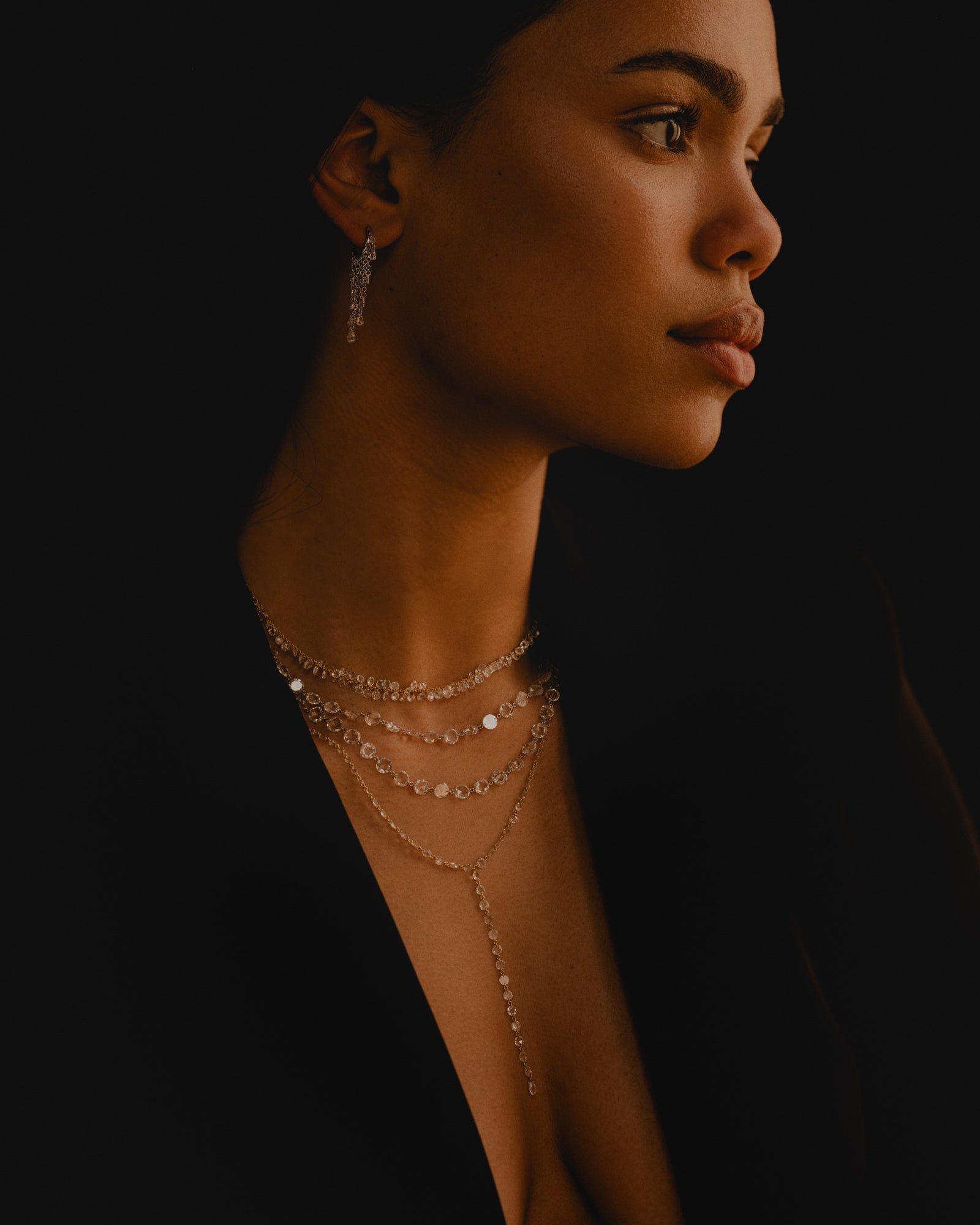 Woman wearing a delicate chain gold and rose cut diamond necklace against a dark background.