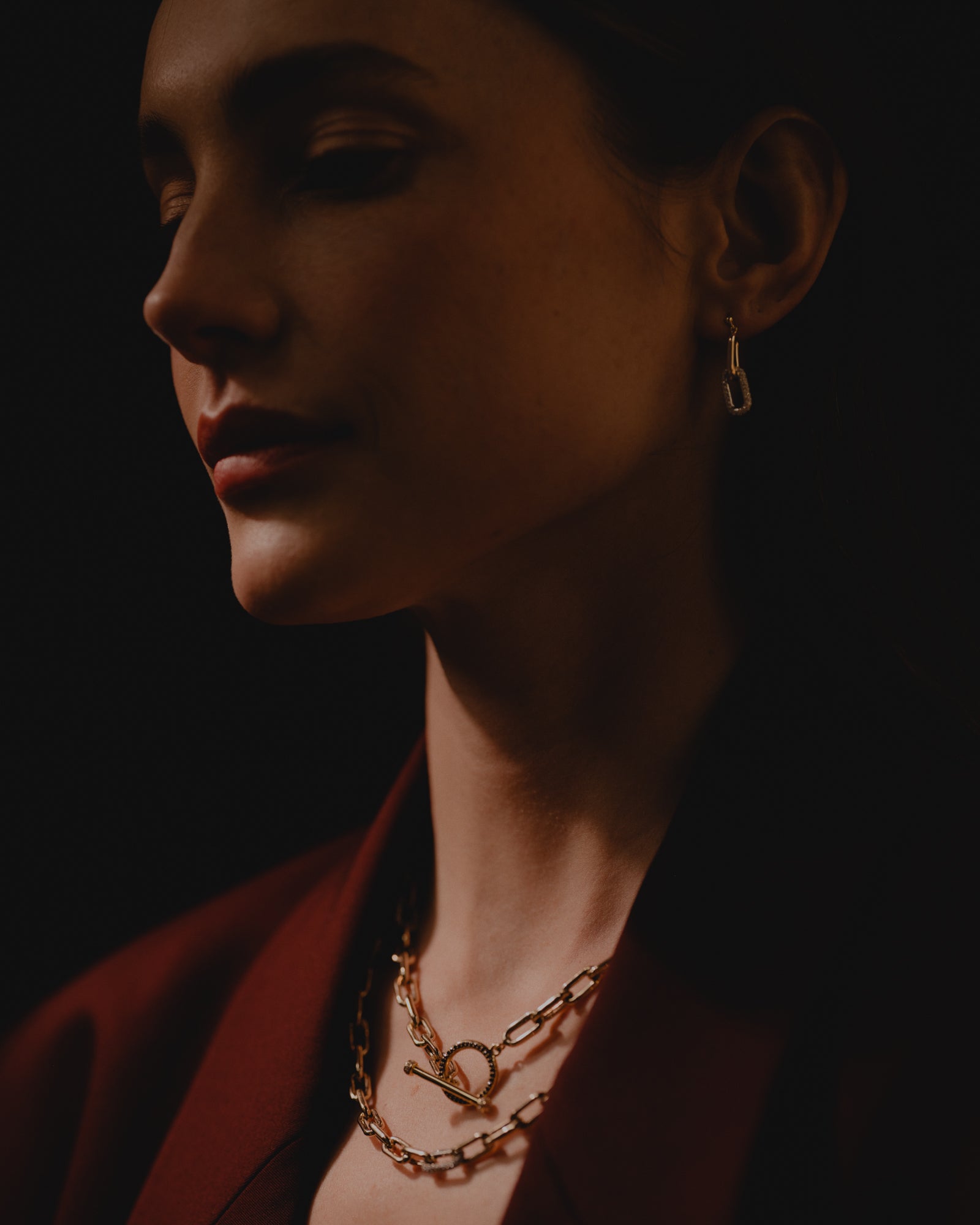 Women dimly lit at photoshoot wearing pieces from Eleuthera Zo Chain collection. 14k yellow gold and diamond link necklaces with blue sapphire toggle. Wearing the matching linked chain earrings with pave diamonds and yellow gold.