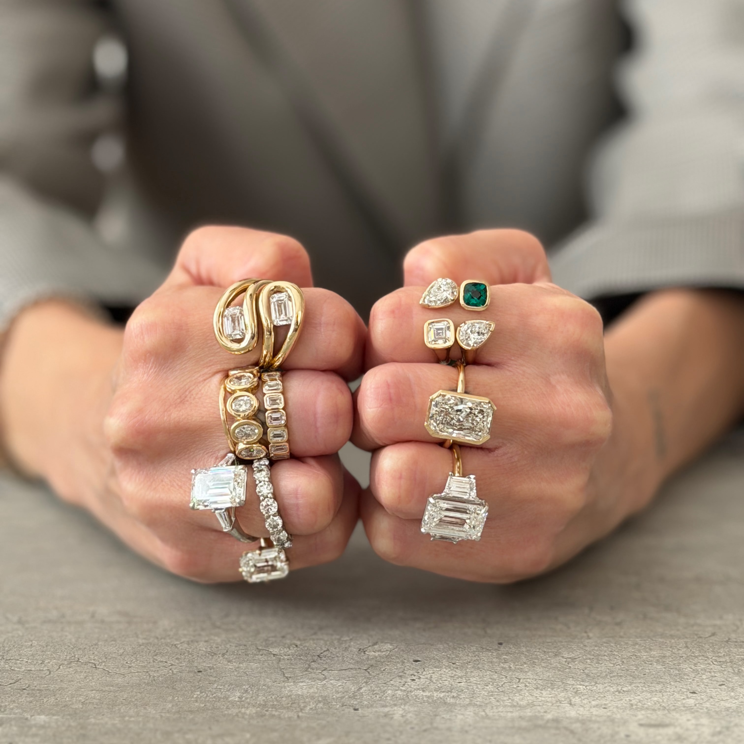 Two hands displaying a variety of rings with different designs and gemstones on a neutral background. 14k Gold and lab diamonds.