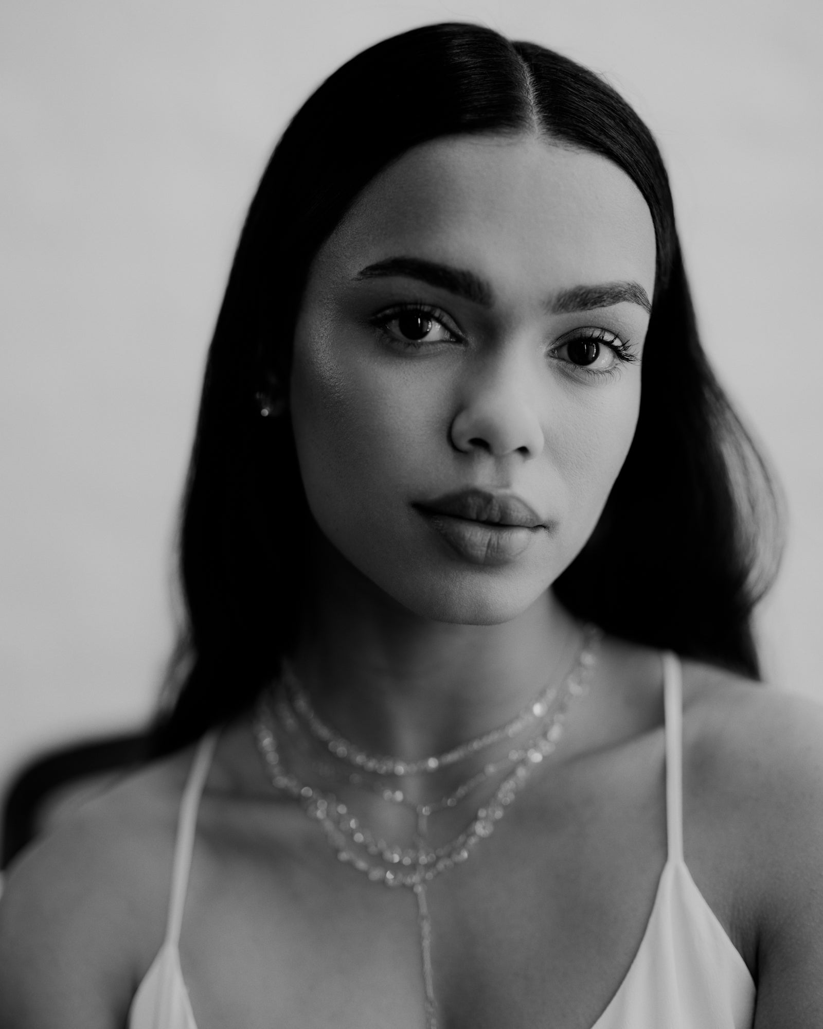 Black and white portrait of a woman wearing a delicate necklace against a plain background. Rose cut diamond and gold  layered necklaces. 