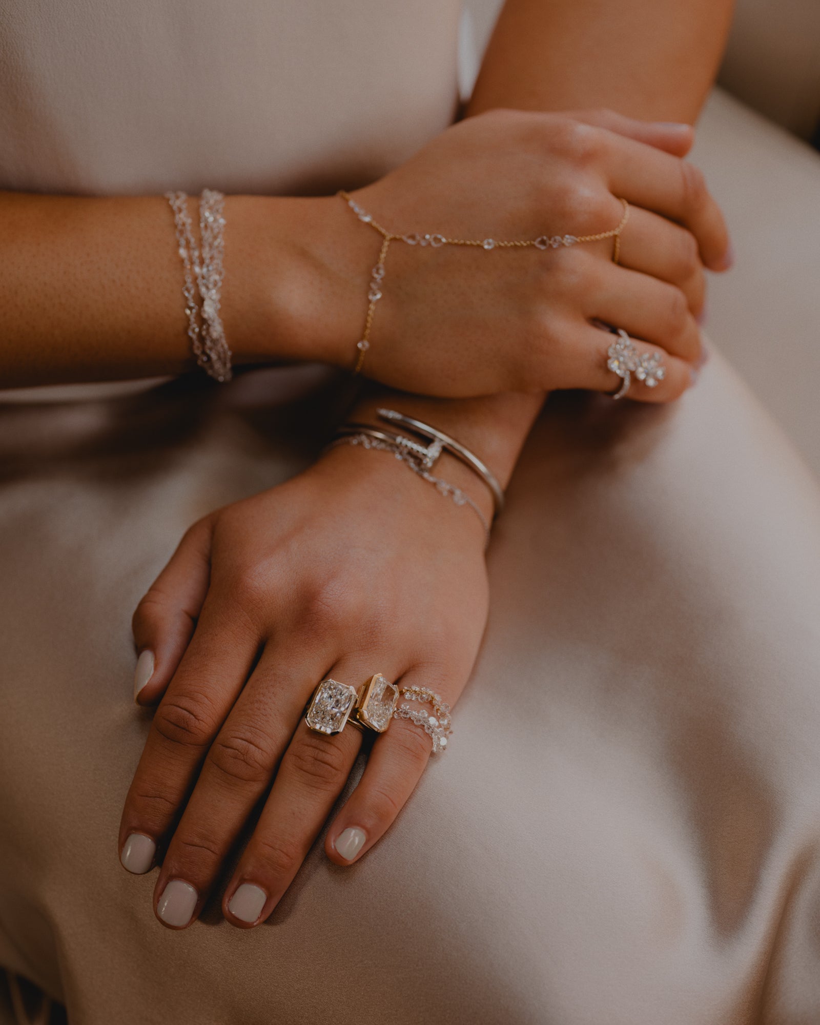 Hands with stacks of dimaond and gold bracelet and rings.  Rose cut diamonds hang off a delicate 18k gold chain rings and 2 8 carat lab dimaond radiant bezel set rings in 14k gold, cartier nail bracelet in white gold, rose cut diamond hand chain, rose cut flower ring on pinky and rose cut multi strand bracelet. 