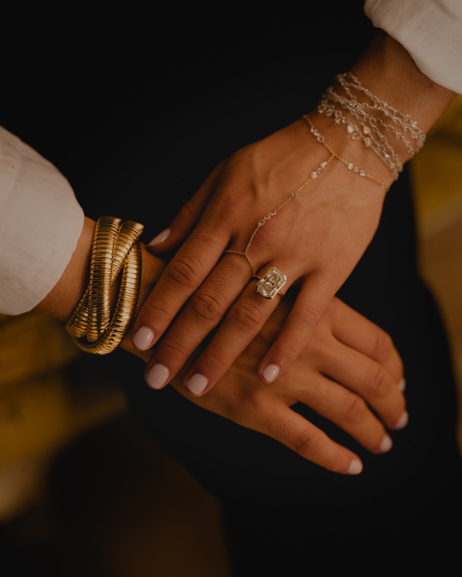 Close-up of hands with gold tubogas bracelet, 8 carat diamond bezel set ring and rose cut hand chains on a dark background