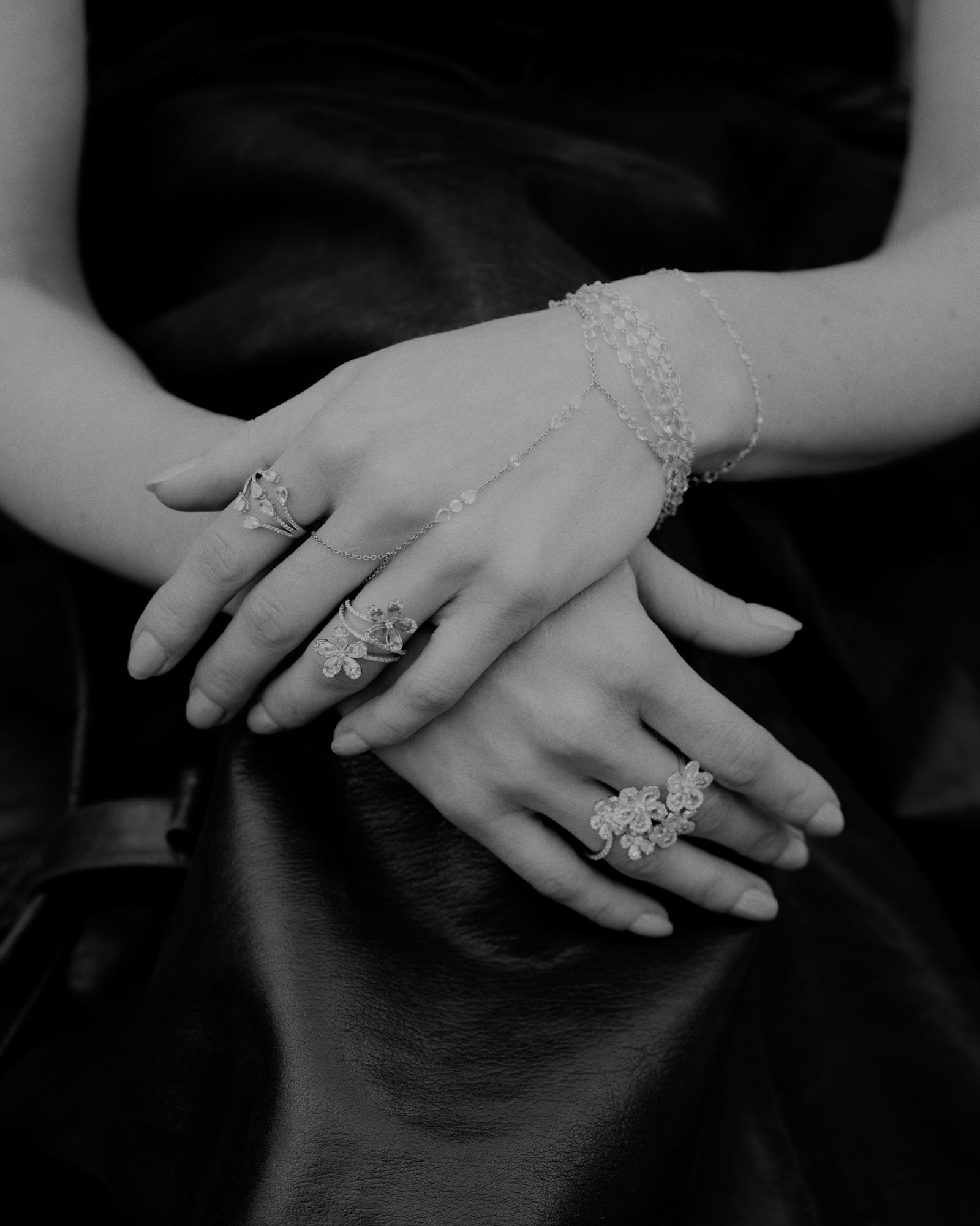 Woman's hand wearing 4 rings made of rose cut natural mined diamonds and emeralds.  A rose cut diamond delicate hand chain drapes down gently layered with multi strand rose cut bracelets. 