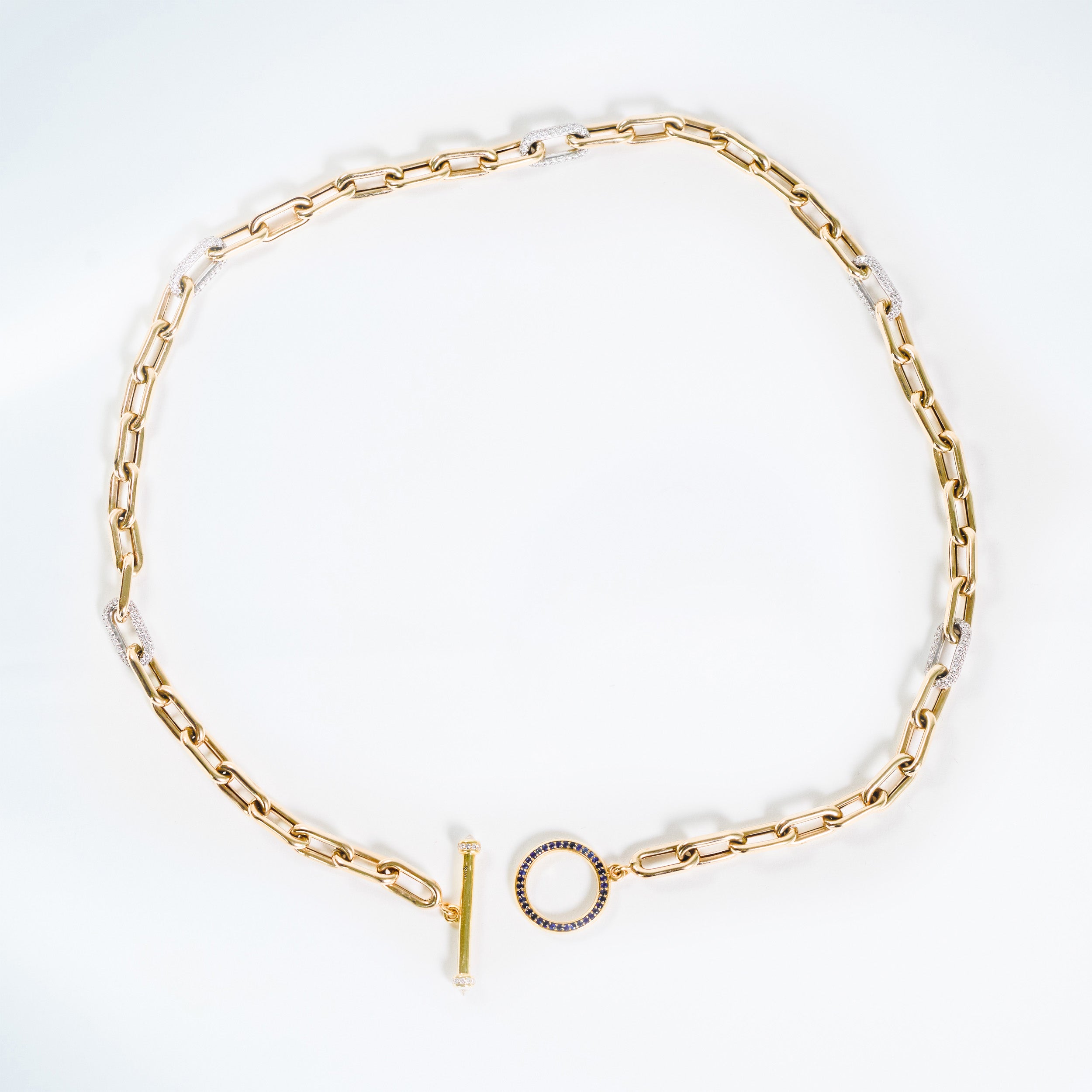 Gold chain necklace on a white background. yellow gold and white pave diamond link chain.  blue sapphire round toggle with pave diamond bar. 