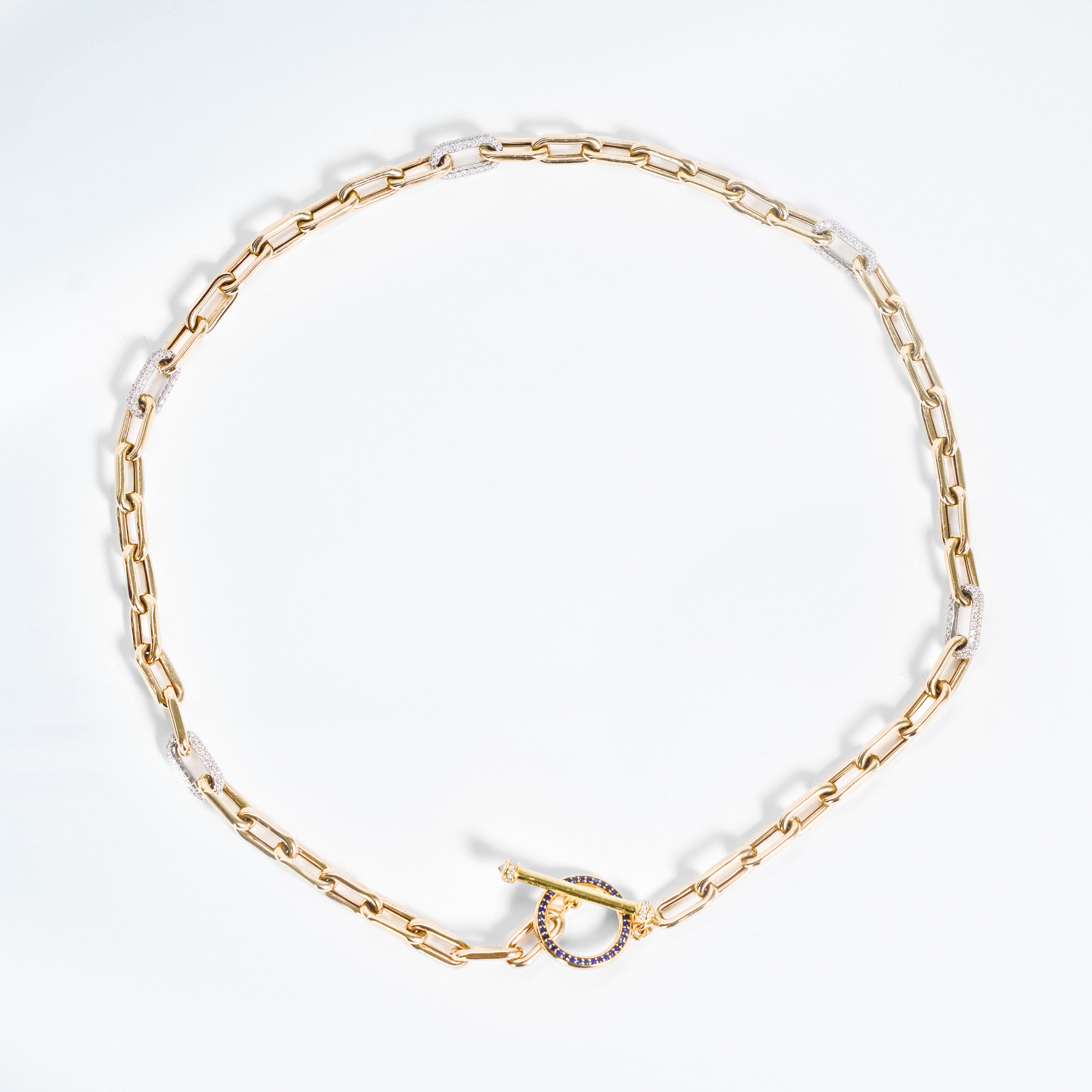 Gold chain necklace on a white background. yellow gold and white pave diamond link chain.  blue sapphire round toggle to close necklace. 