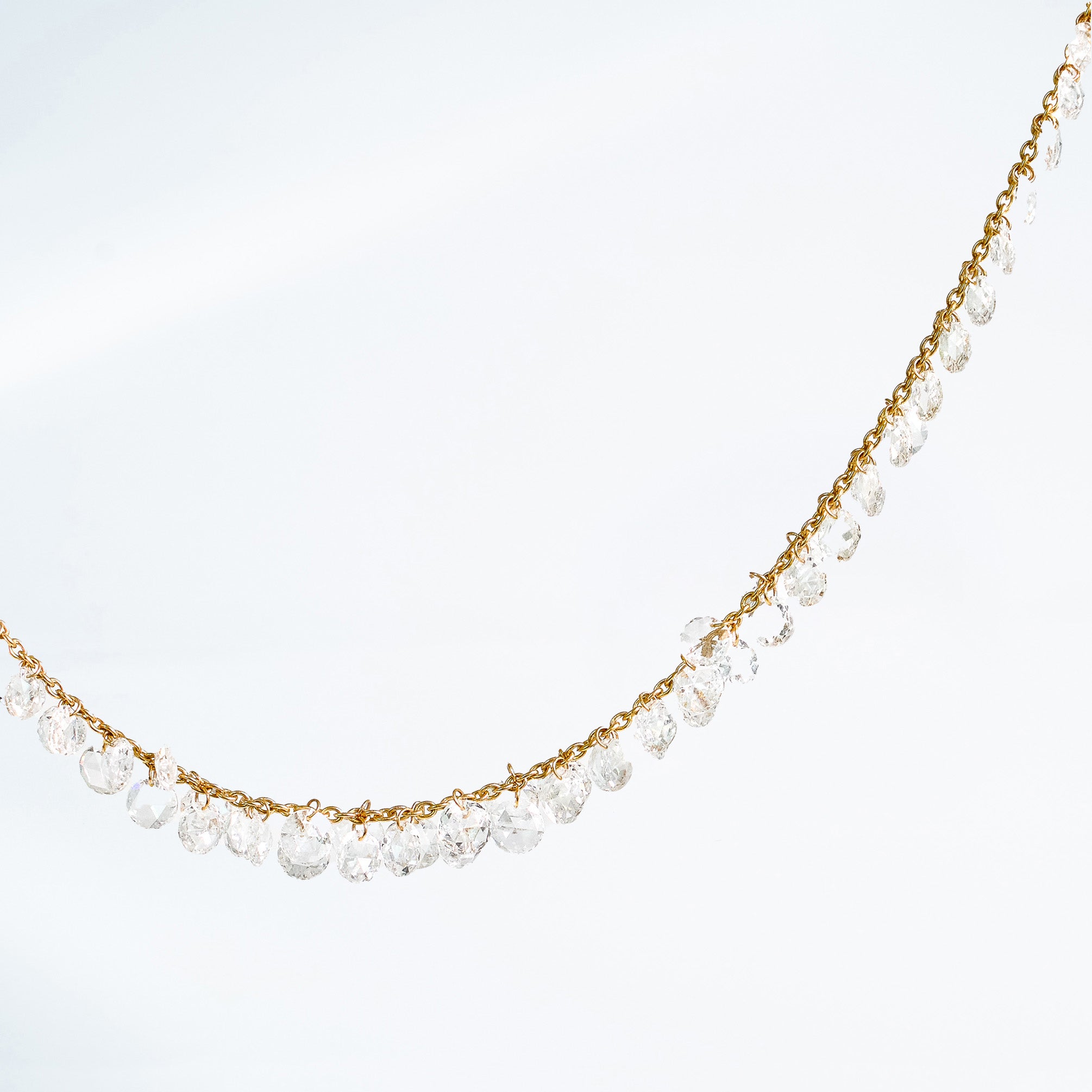 Details on a rose cut diamond necklace set in yellow gold on white background.